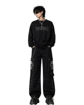 Men's baggy cargo pants in black with skull graphic pockets and chain detail, front view