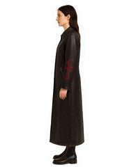 Side view of a black gothic cross leather trench coat with long red cross embroidery on the sleeve, worn by a female model