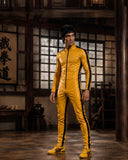 A man wearing a shiny yellow full-body tracksuit with black side stripes and black zipper details, standing in a traditional wooden room with Japanese-style window screens and calligraphy.