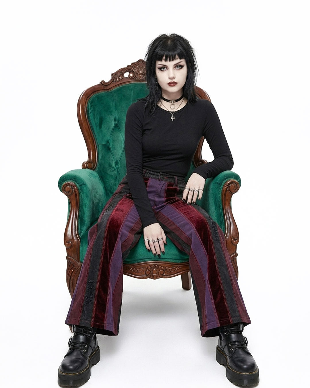 Person sitting on a green velvet chair wearing a black top and red plaid pants.