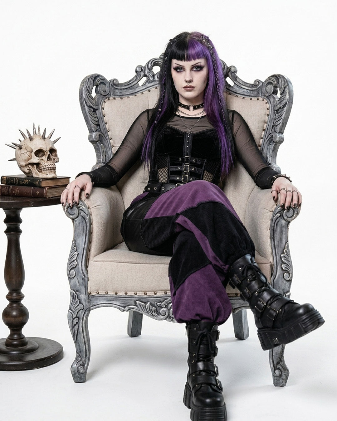 Person in gothic attire sitting on an ornate chair with a skull on a table.