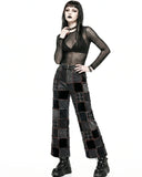 Person wearing a black sheer top and patchwork pants on a white background