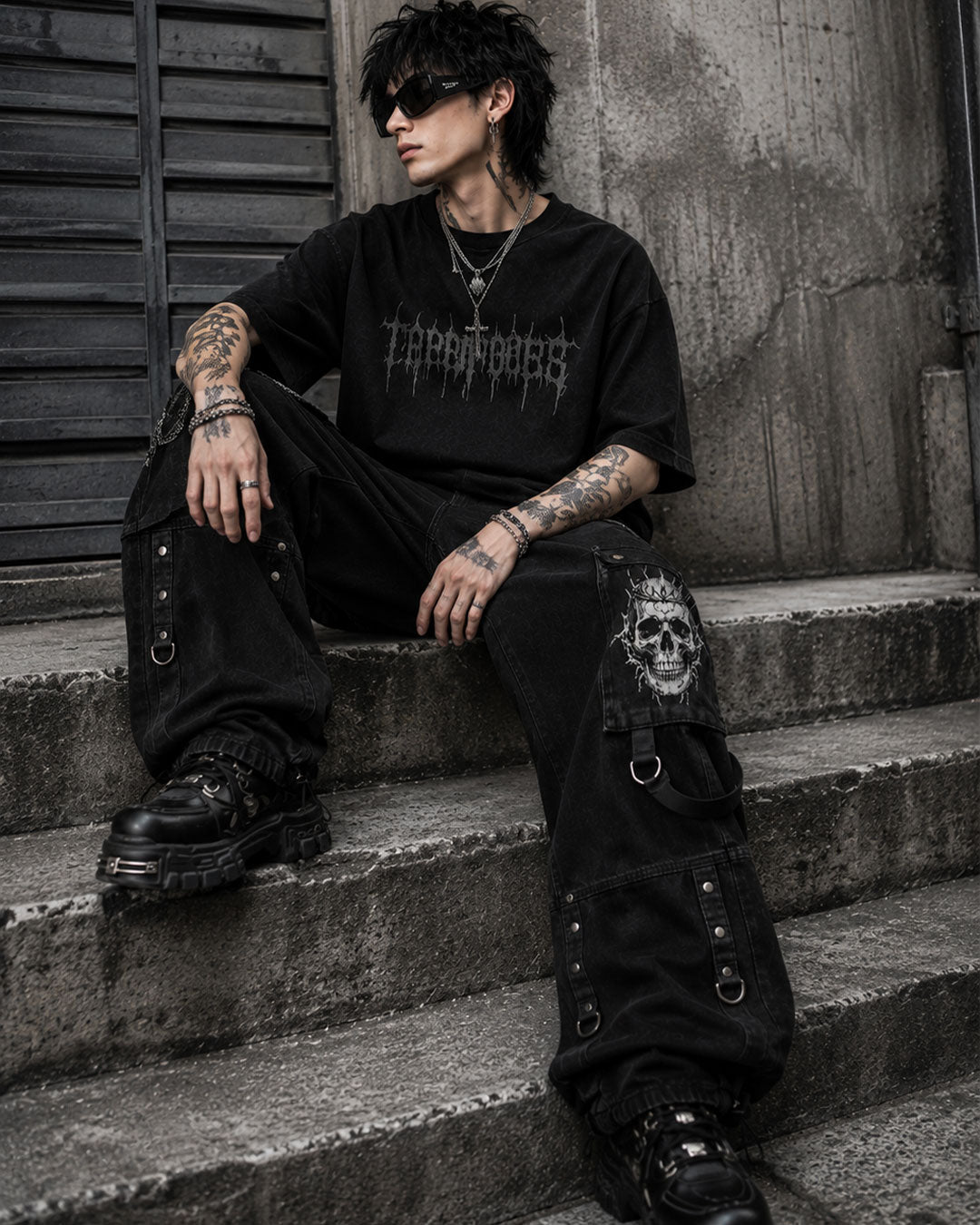 Model sitting in mens wide leg cargo jeans featuring skull print pocket and D-ring straps