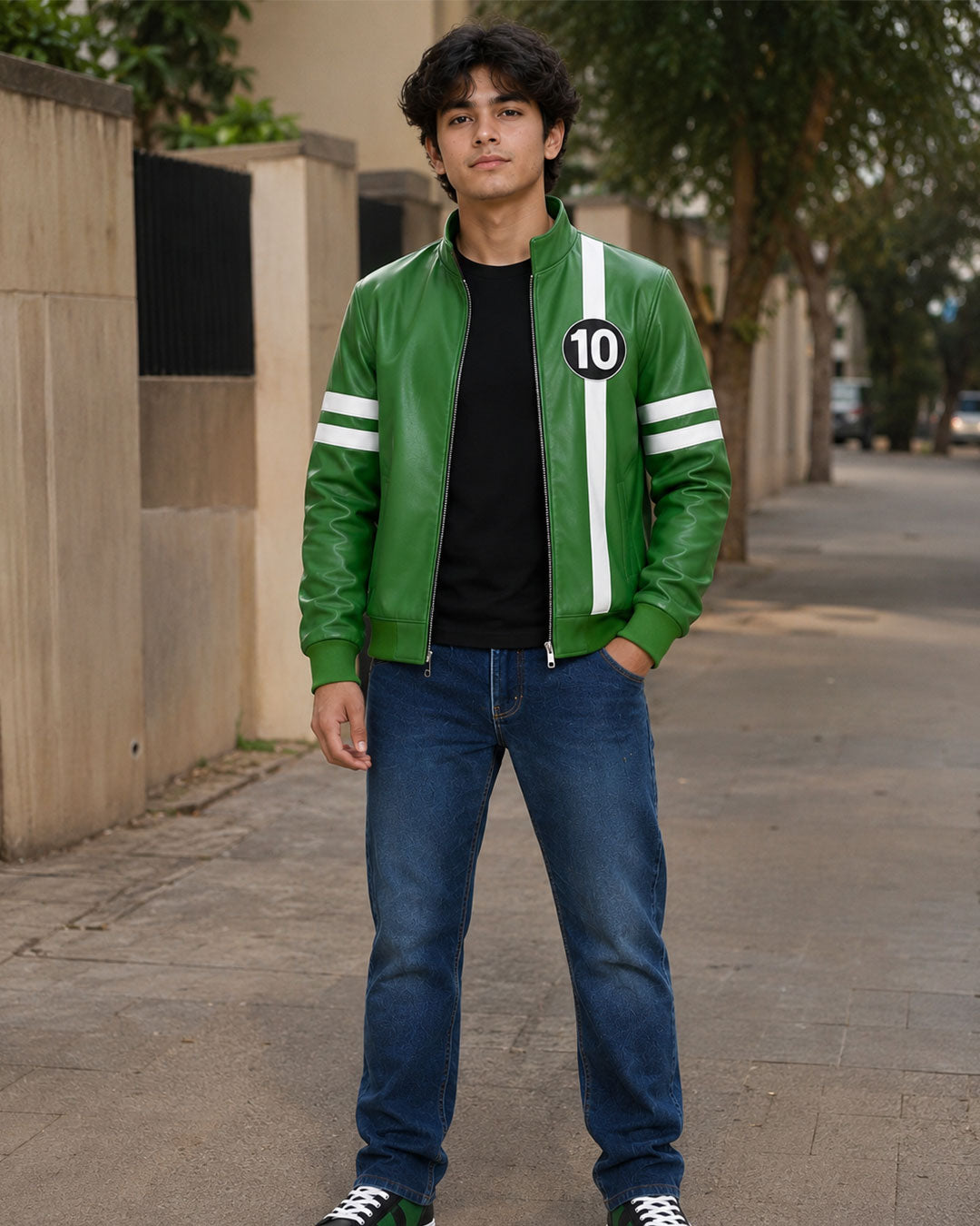 A man wearing a green leather bomber jacket with white stripes and a black number 10 patch, paired with blue jeans and black sneakers, standing on a paved outdoor walkway.