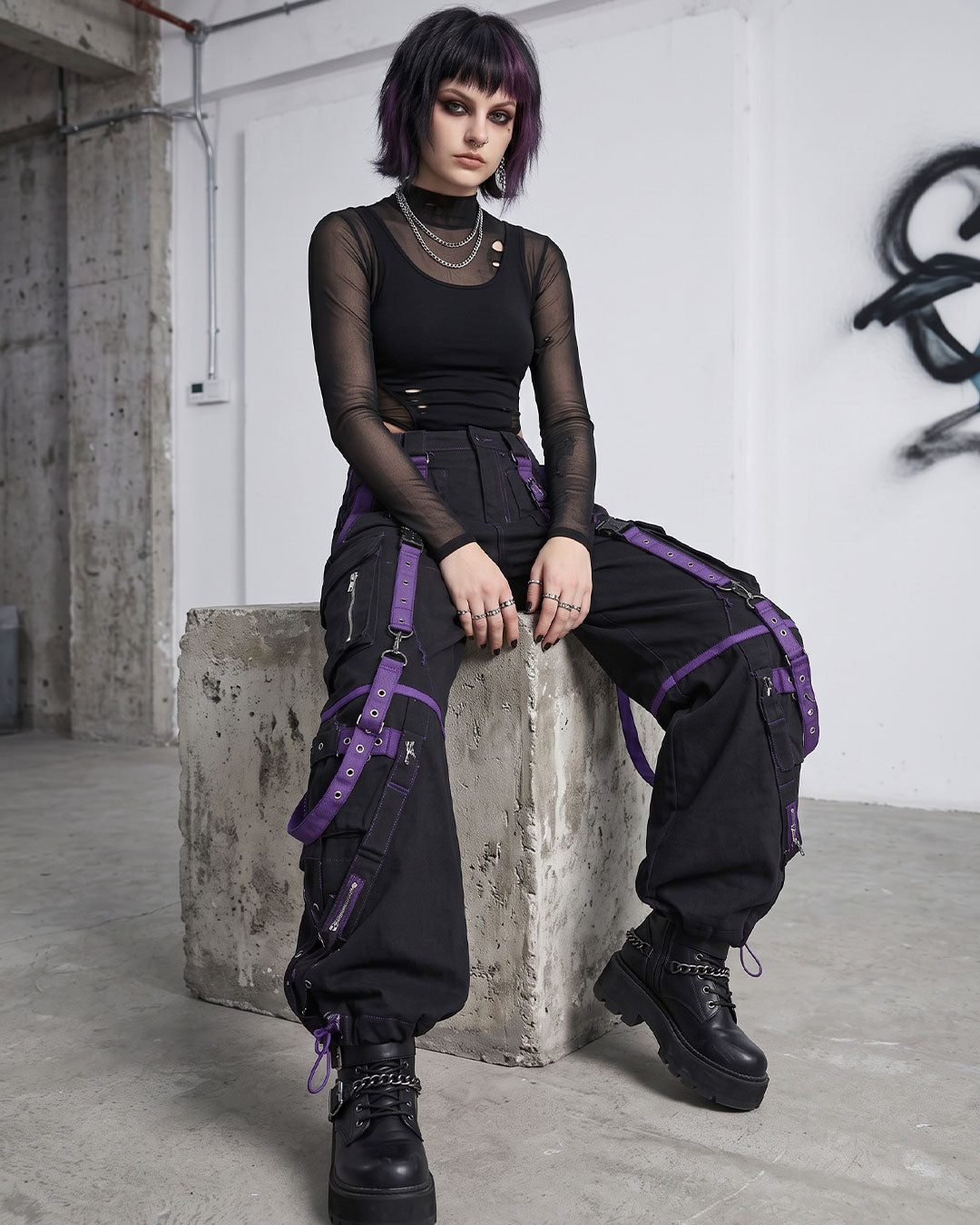 Model sitting in black punk cargo pants with purple buckle straps