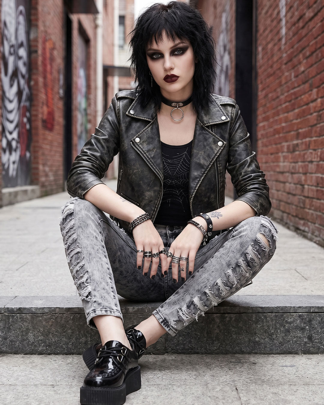 Model sitting on steps wearing ripped jeans women skinny style with grunge leather jacket and platform creepers
