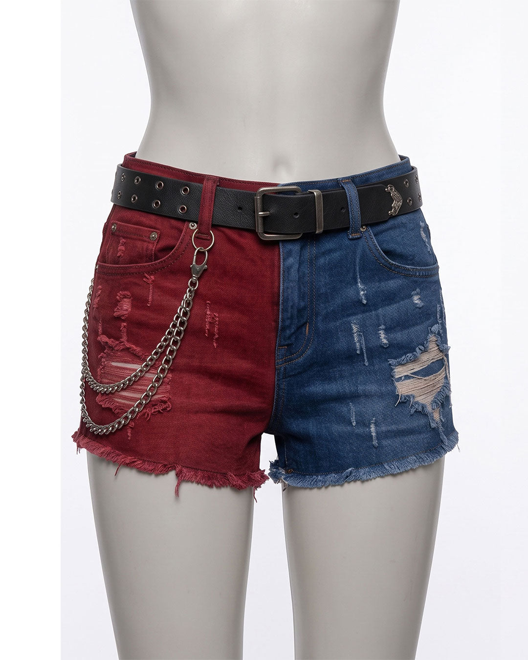 Distressed denim shorts displayed on a mannequin, featuring a split design with faded red denim on the left side and blue denim on the right side, finished with a black studded belt and a hanging silver chain.
