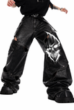 Gothic leather pants for men in black with wide-leg fit, leather-look finish, bold front graphic detail, and oversized alternative streetwear styling shown in lifestyle front and back view.